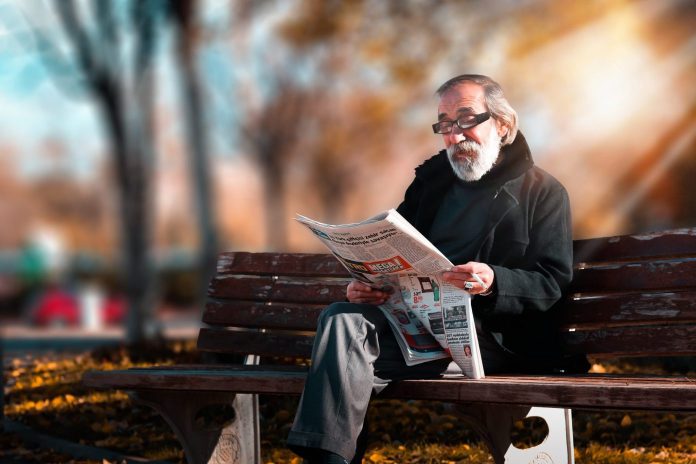 old man reading newspaper in garden