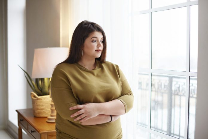 young-female-with-extra-pounds-standing-by-window-home