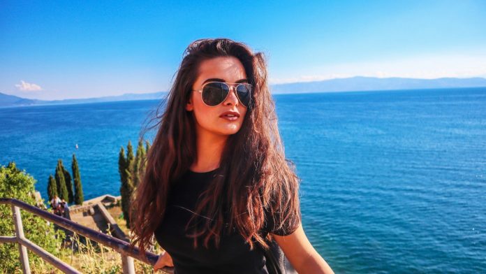 young lady wearing sunglasses with sea in the background