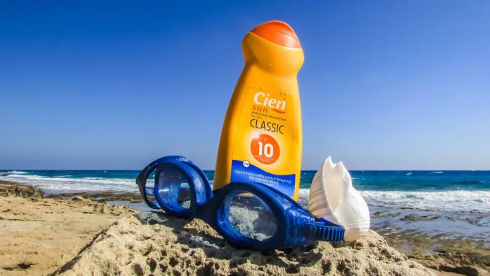 sunscreen bottle and swimming googles lying in the sand on the beach