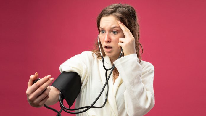 Scared young girl wearing white robe and measuring her own BP with meter